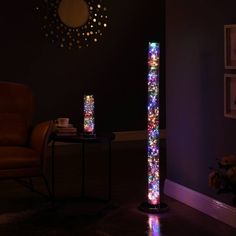 a floor lamp that is lit up with colorful lights in the dark room next to a chair