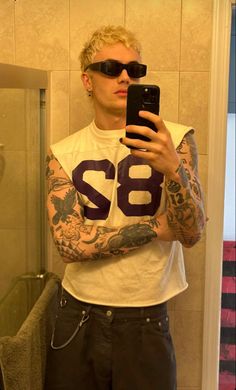 a man with tattoos taking a selfie in the bathroom while wearing sunglasses and holding a cell phone