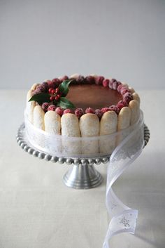 a cake with white frosting and red berries on top is sitting on a silver platter