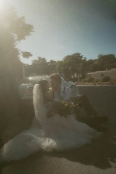 a bride and groom sitting on the ground in front of a truck with sun flares behind them