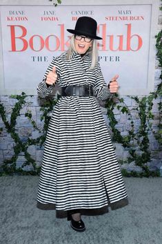 a woman in a black and white striped dress is giving the thumbs up while wearing a hat