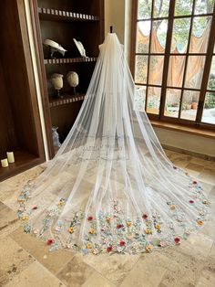 a white wedding veil with flowers on the bottom is hanging in front of a window