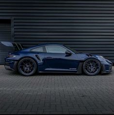 a dark blue sports car parked in front of a garage door with its doors open