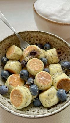 a bowl filled with blueberries and oranges on top of a table next to a cup