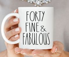 a woman holding a white coffee mug with the words forty fine and fabulous on it