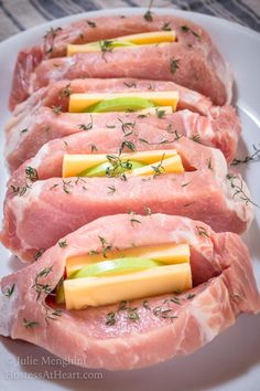 four pieces of raw meat on a plate with cheese and green garnishes