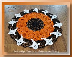 an orange and black crocheted doily with white cats on it, in the shape of a circle