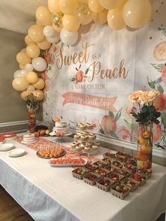 a table topped with lots of food next to a wall covered in balloons and flowers