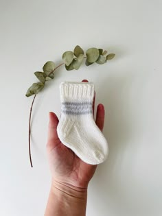 a hand holding a small white sock next to a plant