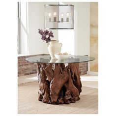 a glass table topped with a vase and two candles next to a tree stump trunk