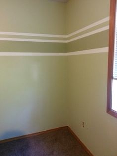 an empty room with green and white stripes painted on the wall next to a window