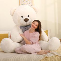 a woman sitting on top of a bed next to a giant teddy bear