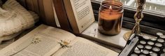 an old typewriter and some books on a window sill next to a candle