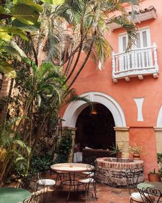 an outdoor patio with tables and chairs next to a pink building that has white balconies on it