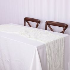 two wooden chairs sitting at a table with a white table cloth on it and one chair facing the table