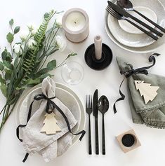 the table is set with black and white plates, napkins, silverware, candlesticks and greenery