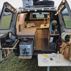 the back end of an rv parked in a field with its doors open and luggage on the floor