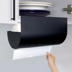 a hand holding a roll of toilet paper in front of a wall mounted dishwasher