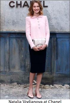 a woman standing in front of a chanel sign wearing a pink sweater and black pencil skirt