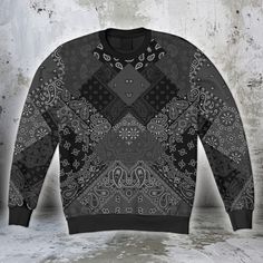 a black and white sweater with an ornate design on the front, sitting against a concrete wall