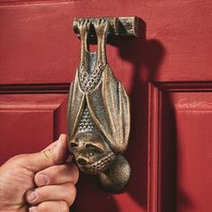 a hand holding an ornate door handle to a red door with a metal object hanging from it's side