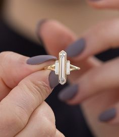 a close up of a person's hand holding a ring with a baguette on it