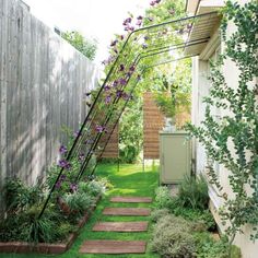 an outdoor garden with steps leading up to the side of a house and flowers growing on the fence