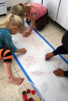 three children are playing with their drawings on the floor in front of some cupboards