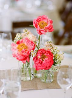 three vases with flowers in them sitting on a dining room table set for an event