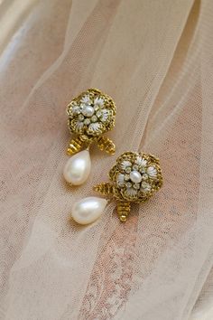 These vintage-inspired wedding earrings bloom with intricate handcrafted lace blossoms. The flower petals are enhanced with ivory silk embroidery, while clusters of vintage crystals sparkle at their centers. A freshwater pearl teardrop hangs from a sprig of hand-beaded leaves, making the a romantic addition to your bridal look. ⁠ ⁠ Handcrafted in our Vermont, USA, studio using old-world lacemaking techniques and heirloom-quality materials. Shop the collection online at ederajewelry.com⁠ White Pearl Drop Bridal Earrings For Reception, Wedding Pearl Drop Earrings In Flower Shape, Handmade Flower Gold Jewelry For Wedding, Gold Handmade Flower Earrings For Wedding, Gold Wedding Earrings With Handmade Flowers, Gold Wedding Jewelry With Handmade Flowers, Handmade Gold Flower Earrings For Wedding, Flower Shaped Clip-on Wedding Jewelry, Traditional Handmade Flower Jewelry For Wedding