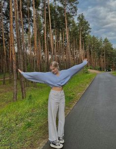 a woman standing on the side of a road with her arms outstretched in front of trees