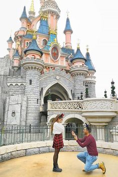 a man kneeling down next to a woman in front of a castle