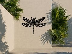 a black dragonfly sitting on the side of a wall next to palm trees and plants