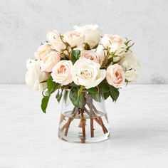 a vase filled with white and pink roses on top of a marble countertop next to a wall