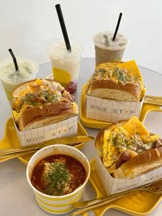 four different types of food sitting on yellow trays with spoons and cups in front of them