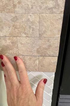 a woman's hand with red nail polish on her nails next to a tile wall