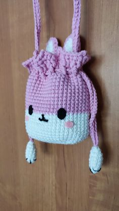 a crocheted pink and white hat hanging on a wooden wall with black eyes