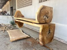 a wooden bench sitting on top of a cement floor next to a white wall and tree stumps