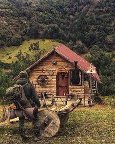 a man with a backpack is carrying a large wheel barrow in front of a log cabin