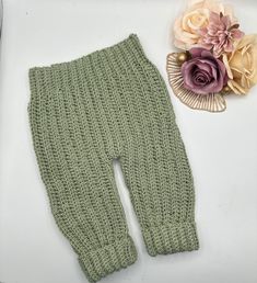 a green knitted leggings next to a flower on a white surface with a pink rose