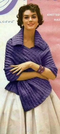 a woman in a purple sweater and white dress with her arms crossed, posing for the camera