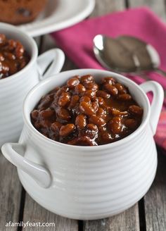 two white bowls filled with baked beans on top of a wooden table