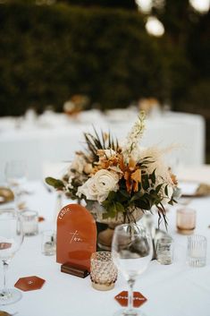 an arrangement of flowers in a vase on top of a table with wine glasses and place settings