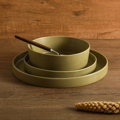 three bowls and two spoons on a wooden table with a piece of bread next to them