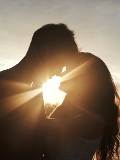 a man and woman kissing in front of the sun