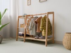 a wooden rack with clothes on it next to a potted plant in a room