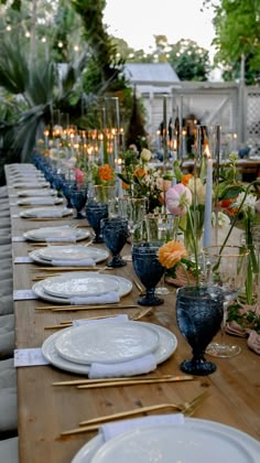 a long table is set with white plates and blue vases