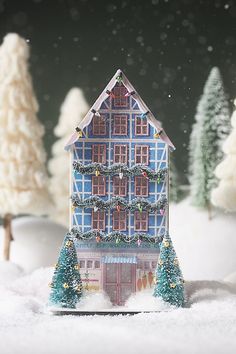 a miniature house is in the snow with christmas decorations on it's roof and trees