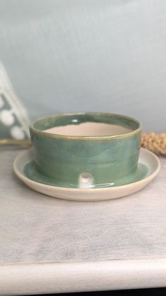 a green cup and saucer sitting on a white counter top next to a pillow