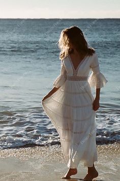 a woman in a white dress walking on the beach